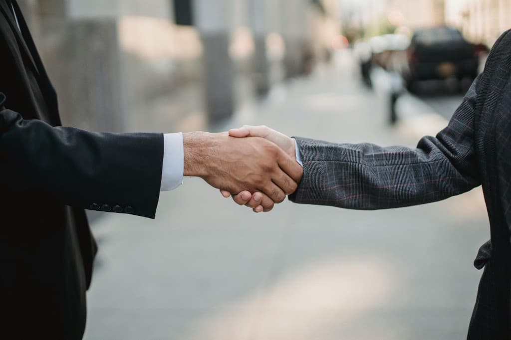 Firm professional handshake between two people in business attire outdoors